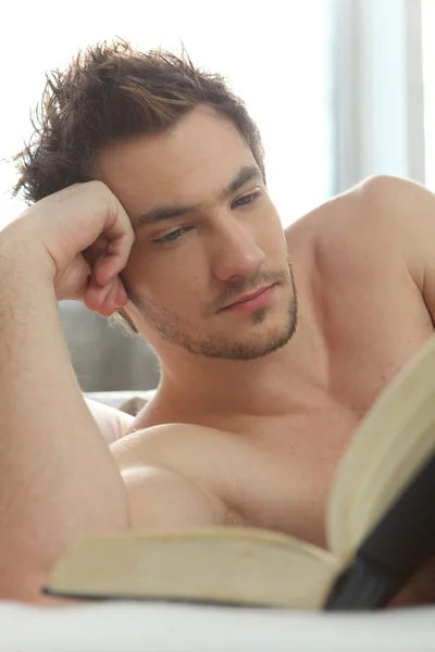 Fiatal férfi az ágyban egy könyvet olvas — Stock Fotó
