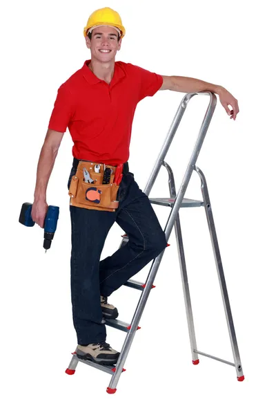 Человек с дрелью стоит на ступени лестницы — стоковое фото