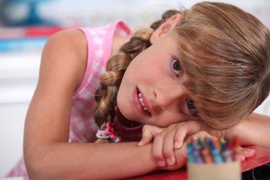 Little girl with crayons resting head on desk clipart