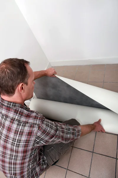 Crouching man unrolling flooring — Stock Photo, Image