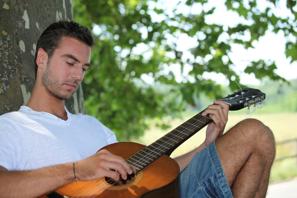 माणूस झाडाखाली गिटार वाजवतो — स्टॉक फोटो, इमेज