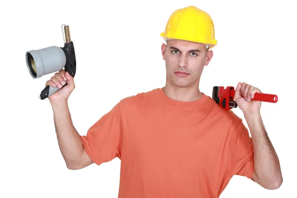 Tradesman holding a pipe wrench and a blowtorch — Stock Photo, Image