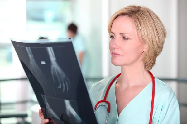 Woman in scrubs examining X-rays — Stock Photo, Image