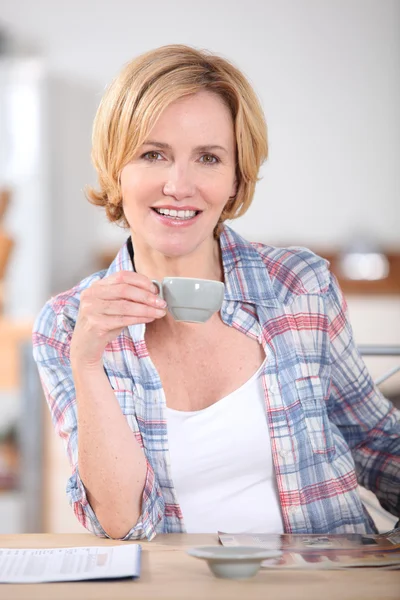 Vrouw met kopje koffie bij keukentafel — Stockfoto