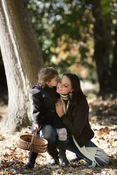 Kleines Mädchen küsst ihre Mutter im Wald — Stockfoto