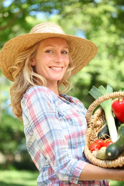 Mulher sorrindo com um chapéu de palha segurando cesta de legumes . — Fotografia de Stock