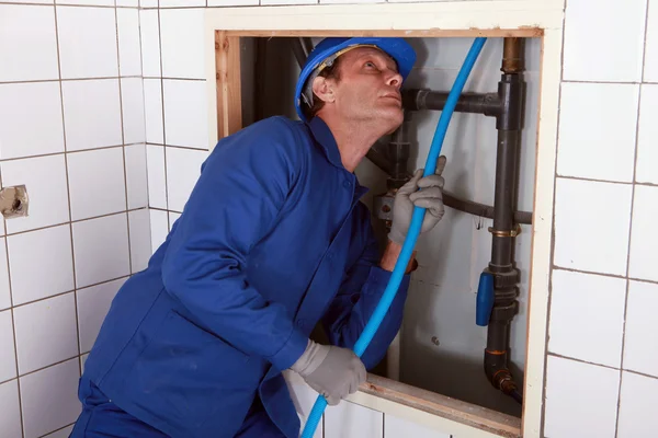 Plombier alimentant tuyau bleu derrière un mur — Photo