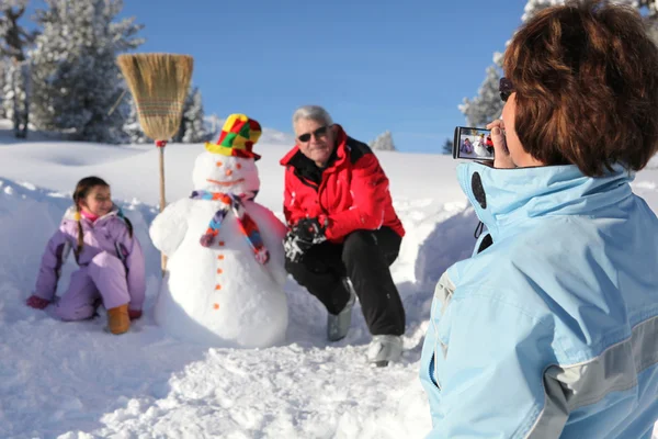 Avó tirando uma foto de sua família e seu boneco de neve — Fotografia de Stock