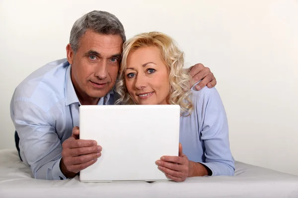 Mellersta äldre par med en laptop på deras säng. — Stockfoto