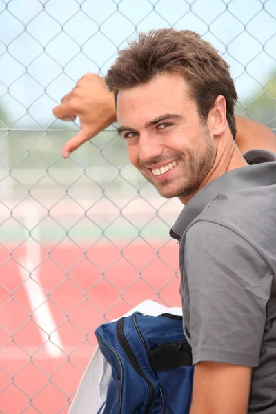 Jugador de tenis sonriente parado fuera de una pista dura — Foto de Stock