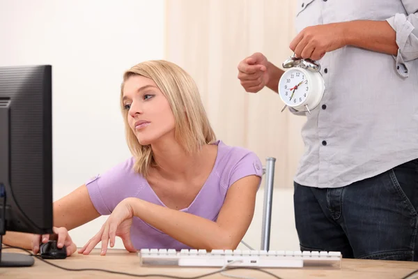 A young blonde woman is doing computer and a man is showing an alarm clock — Stock Photo, Image
