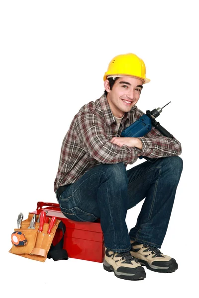 Unga hantverkare innehar en borr och sitter på en verktygslåda — Stockfoto