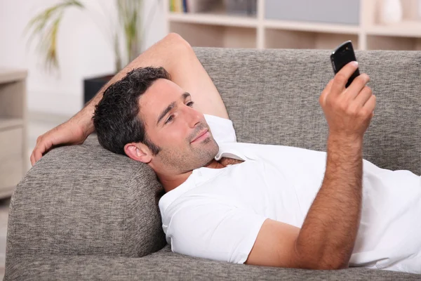 Amüsierter Mann, der auf dem Sofa liegt und eine SMS schickt — Stockfoto