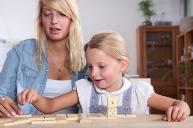 Young woman and her daughter playing dominoes clipart