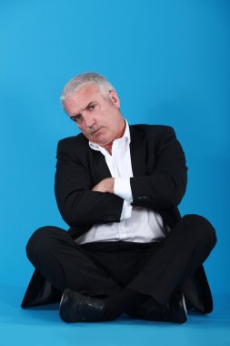 Middle-aged man sitting cross-legged and cross-armed against blue backgroun clipart
