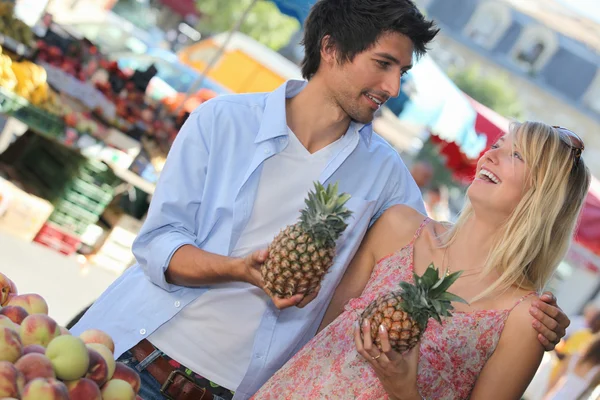Casal jovem segurando abacaxis em uma barraca de mercado — Fotografia de Stock