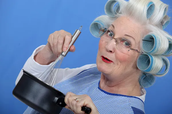 Cheeky older woman in rollers whisking sauce — Stock Photo, Image