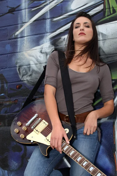 Fajne gitarzysta kobieta stojąc przed graffiti — Zdjęcie stockowe