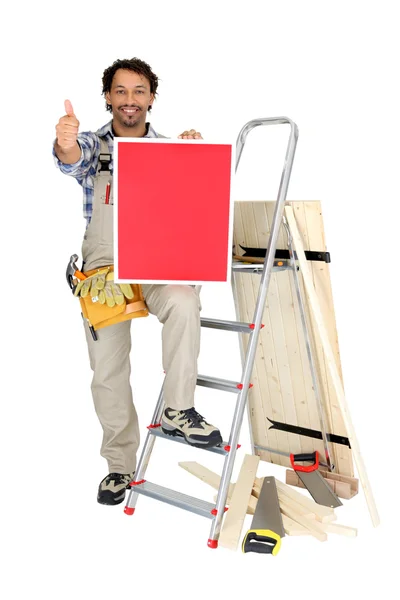 Um carpinteiro fazendo polegares para cima e mostrando um painel vermelho — Fotografia de Stock