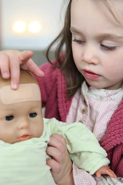 Petite fille mettant un plâtre sur le front de sa poupée — Photo