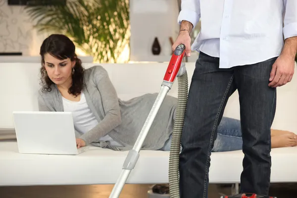 掃除機をかける男と彼女のラップトップに取り組んでいる女性 — ストック写真