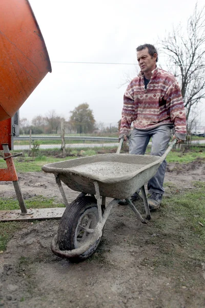 Uomo che trasporta cemento in carriola — Foto Stock