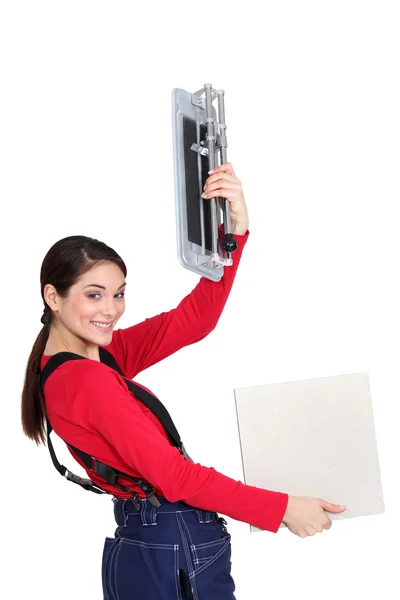 Tradeswoman holding up a tile cutting machine and a tile — Stock Photo, Image