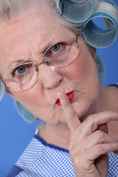 Ηλικιωμένη γυναίκα με τα μαλλιά της σε κυλίνδρους, κρατώντας το δάχτυλό της μέχρι τα χείλη της — Φωτογραφία Αρχείου