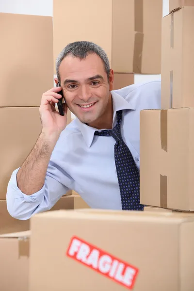40-45 Jahre alter Angestellter ruft jemanden in einem Raum voller Kartons an — Stockfoto