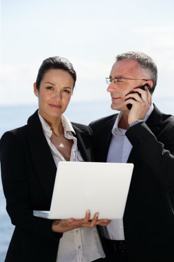 Businesswoman with laptop next to a collaborator on phone clipart