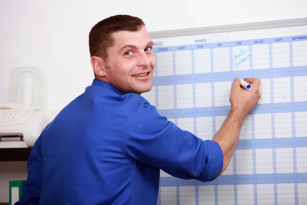 Pracownik ubrany w niebieski jumpsuite pisze w kalendarzu — Zdjęcie stockowe