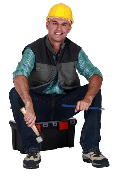 Comerciante sonriente sentado en su caja de herramientas y sosteniendo herramientas —  Fotos de Stock