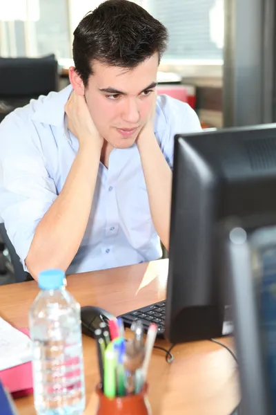 Fiatal ember tartja a nyakát egy asztali számítógép előtt — Stock Fotó