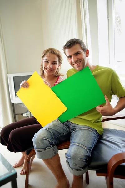 Couple sat at home holding colorful posters — Stock Photo, Image