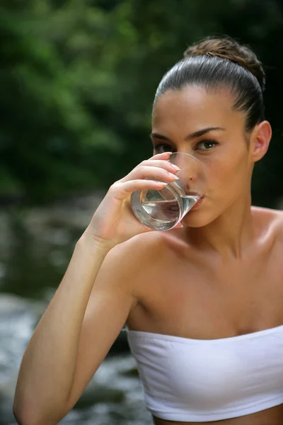 Женщина пьет стакан воды у реки — стоковое фото