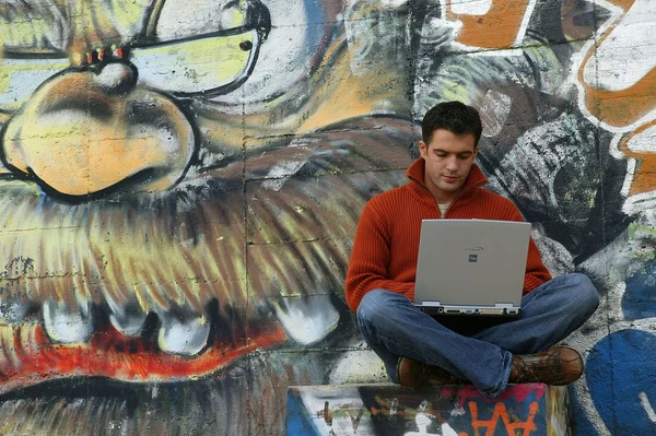 Hombre con portátil sentado por la pared gratificada —  Fotos de Stock
