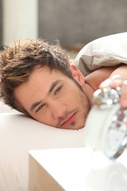 Bleary eyed man looking at his alarm clock clipart