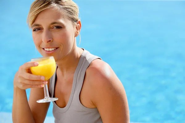 Mulher loira desfrutando de suco de laranja por piscina — Fotografia de Stock