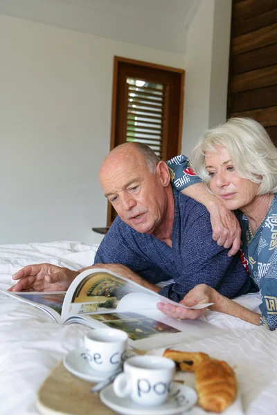 Старша пара дивиться на журнал в ліжку — стокове фото