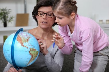 Little girl looking at a globe with her grandmother clipart