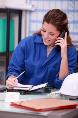 Woman wearing blue overalls speaking on telephone clipart