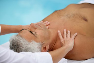 Mature man being massaged next to a swimming pool clipart