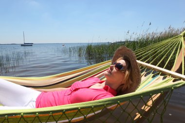 Woman in straw hat relaxing on a hammcock clipart