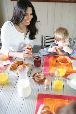 Mother and son eating breakfast at the table clipart