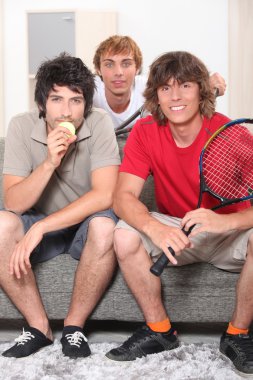 Guys sitting on sofa with tennis rackets clipart