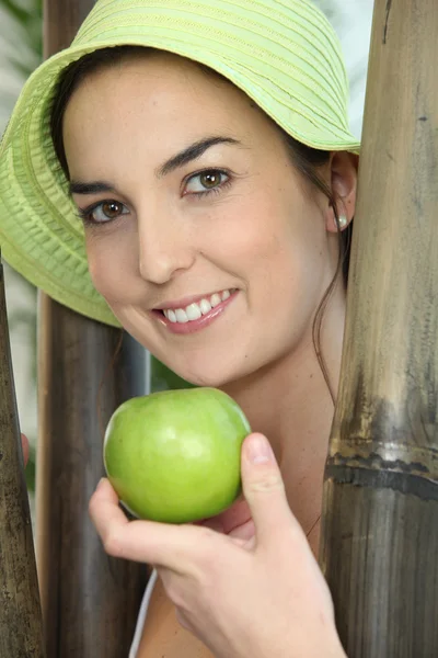 Mulher ficou ao lado de postes de madeira segurando uma maçã verde — Fotografia de Stock