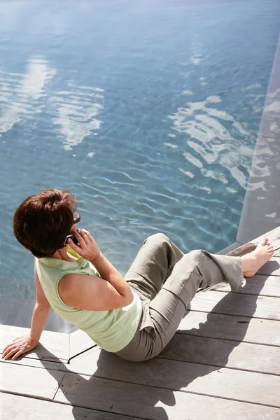 Senior woman sitting by the pool — Stock Photo, Image