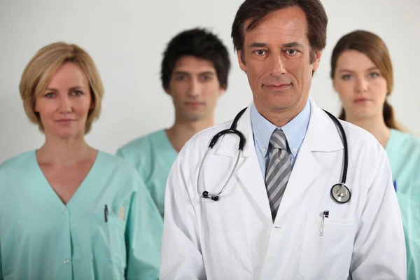 En läkare och tre sjuksköterskor bakom honom, alla tittar på oss. — Stockfoto