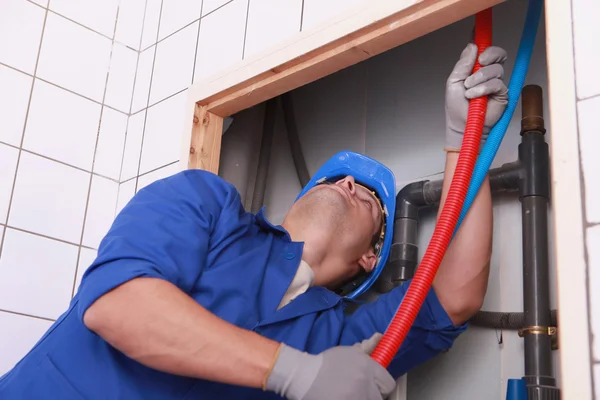 Encanador alimentando tubos flexíveis atrás de uma parede de azulejos — Fotografia de Stock