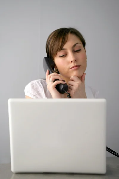 Женщина смотрит на свой ноутбук, разговаривая по телефону — стоковое фото